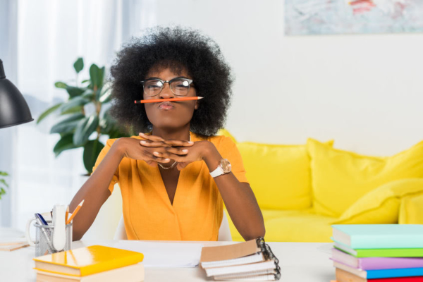Woman sitting at table with a pencil between her nose and upper lip.