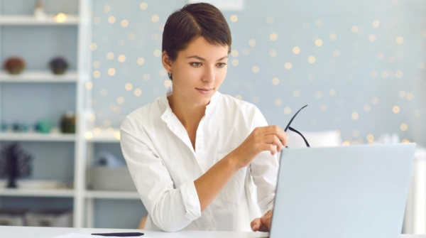 Young professional writer holding a pair of glasses as she works on a laptop..