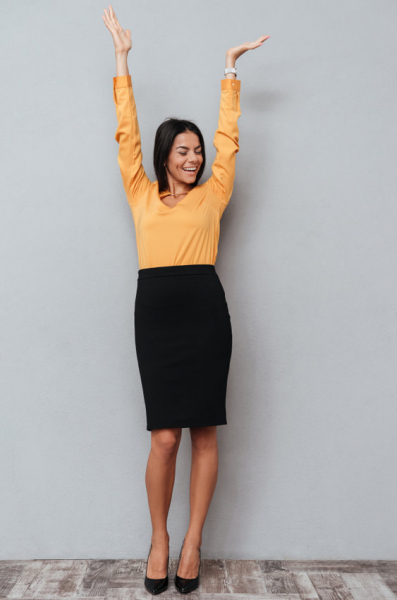 A happy cheerful business woman celebrating success with hands raised