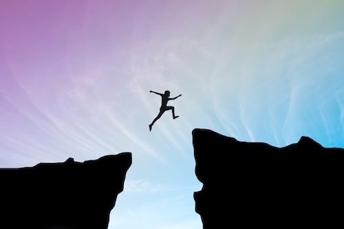 Person jumping over the gap between 2 cliffs.