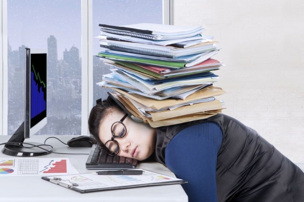 Female entrepreneur feels tired with pile of documents over head while sleeps on the desk, winter background on the window