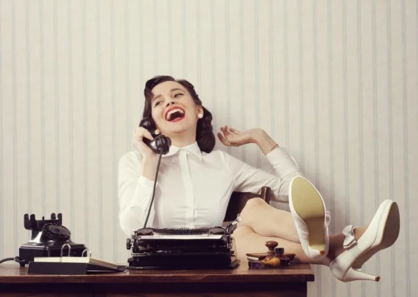 Cheerful woman talking on phone at desk.