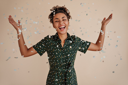 Positive african american woman smiling under confetti. Studio shot of good-humoured black girl expressing happiness.